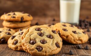 Cookies com Gotas de Chocolate dourados e apetitosos sobre mesa rústica, mostrando textura perfeita e gotas derretidas de chocolate meio amargo.